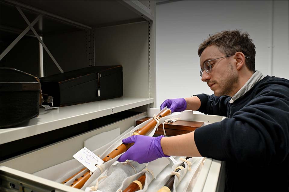 A member of staff holding a flute in storage in the RCM's Wolfson Centre